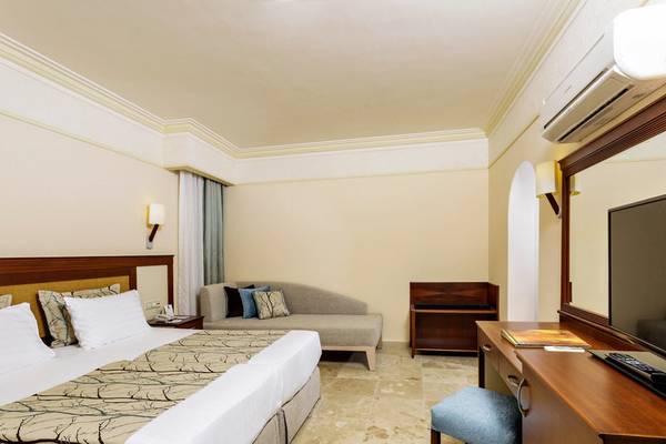 Hotelzimmer im Melas Holiday Village mit Bett, Sofa, Schreibtisch und Fernseher.