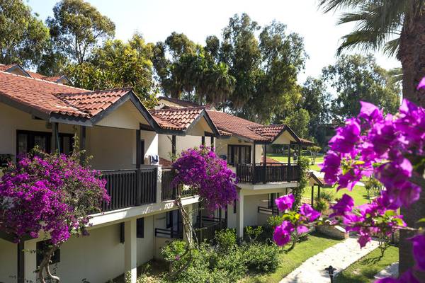 Außenansicht der Melas Holiday Village Bungalows mit roten Dächern und blühenden Büschen