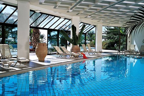 Der Poolbereich des Constantinou Bros Athena Beach Hotels mit Sonnenliegen und Pflanzen.