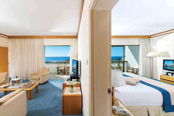 Zimmer im Constantinou Bros Athena Beach Hotel mit Meerblick, Bett, Sofa, Tisch und Fernseher.