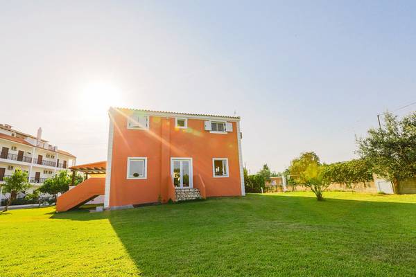 Außenansicht des Bruskos Hotel & Suites, ein orangefarbenes Gebäude mit grünem Rasen und Sonnenlicht.