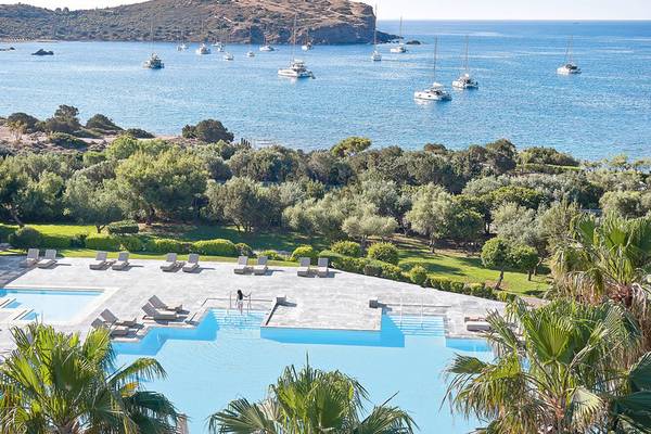 Aussicht auf den Poolbereich des Cape Sounio Grecotel Resorts mit vielen Liegestühlen und Booten im Meer