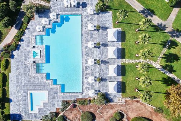 Luftaufnahme des Swimmingpools im Cape Sounio Grecotel Resort mit umliegenden Sonnenschirmen und Rasen.