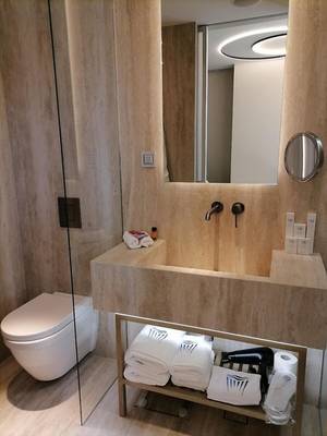 Badezimmer im Hellenic Vibes Smart Hotel in Athen mit Marmorboden, Glasdusche, Toilette, Waschbecken und Toilettenartikeln.
