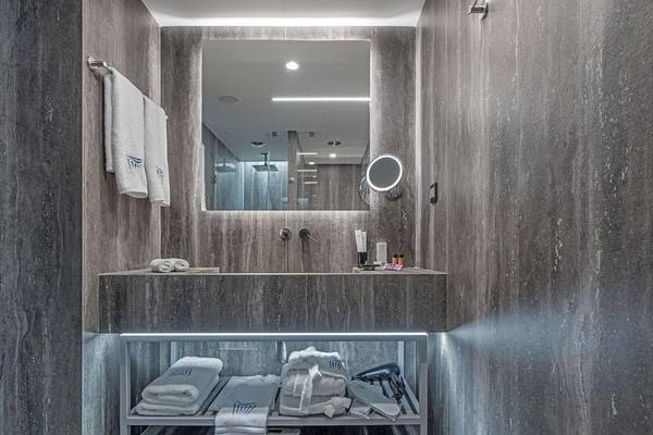 Das Badezimmer des Hellenic Vibes Smart Hotel in Athen mit grauen Wänden, einem Waschbecken, Handtüchern und einem Spiegel.