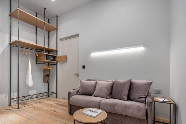 Inneneinrichtung eines Zimmers im Hellenic Vibes Smart Hotel in Athen mit einem Sofa, Tisch, Kleiderständer und einer beleuchteten Wand.