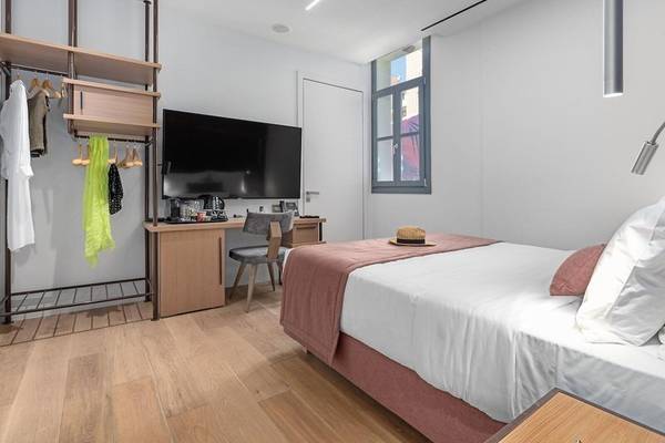Innenansicht eines Zimmers im Hellenic Vibes Smart Hotel in Athen mit Doppelbett, Fernseher, Schreibtisch und Kleiderständer.