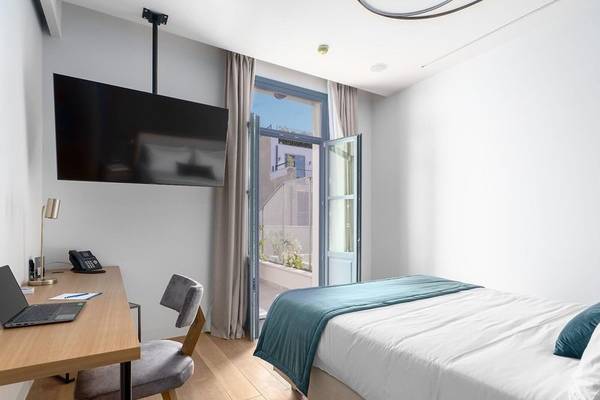 Zimmer im Hellenic Vibes Smart Hotel Athen mit Schreibtisch, Laptop, Telefon und Bett.