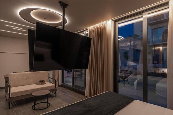 Innenansicht des Schlafzimmers im Hellenic Vibes Smart Hotel in Athen mit Fernseher an der Decke, Sofa und Tisch.