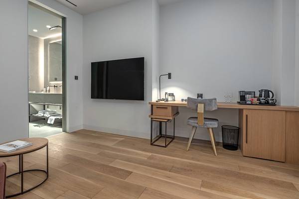 Innenansicht des Zimmers im Hellenic Vibes Smart Hotel Athens mit Schreibtisch, Fernseher und Badezimmereingang.