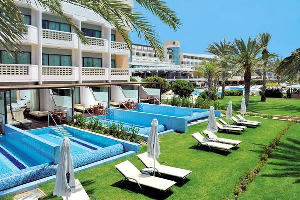 Außenbereich des Constantinou Bros Athena Beach Hotels mit Swimmingpools, Sonnenliegen und Palmen