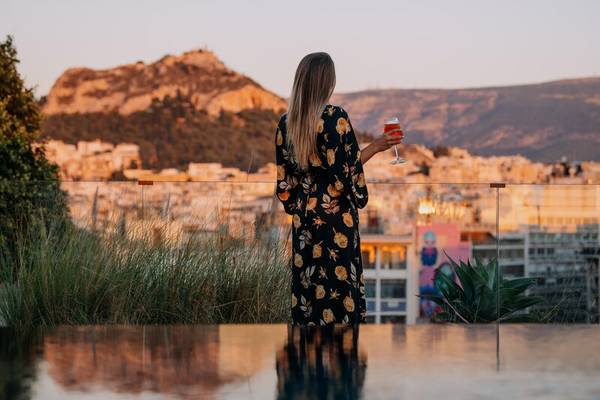 Frau auf Hotelterrasse mit Aussicht auf die Stadt beim Sonnenuntergang.