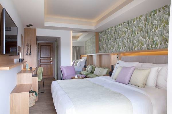 Innenansicht des Schlafzimmers im Dolce Athens Attica Riviera Hotel mit großem Bett, Kissen und Fernseher.