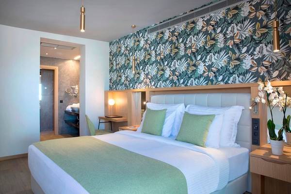 Doppelbett im Hotelzimmer von Dolce Athens Attica Riviera mit grün-weißer Bettwäsche und grünen Kissen.