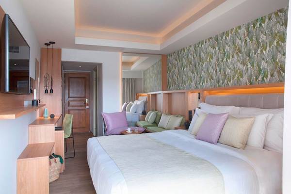 Schlafzimmer im Dolce Athens Attica Riviera Hotel mit großem Bett, Kissen, Fernseher und Wandmuster.