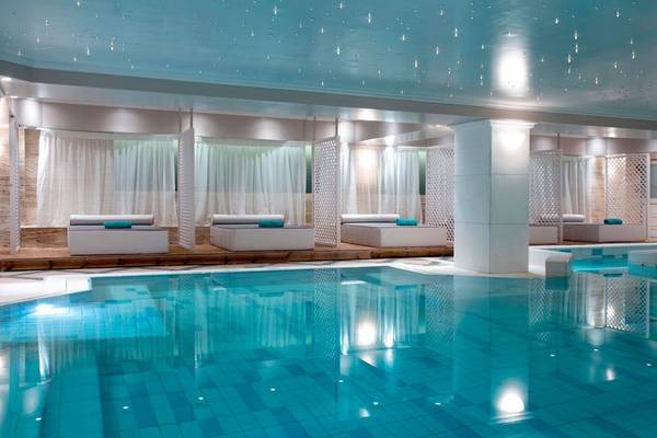Das Dolce Athens Attica Riviera Hotel zeigt sein Schwimmbad mit Loungebereich und Liegebetten.
