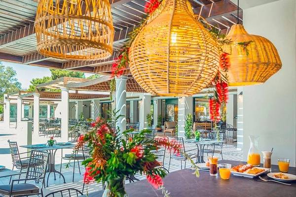 Terrasse des Dolce Athens Attica Riviera Hotels mit Tischen, Stühlen und Blumendekoration.