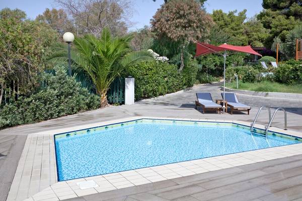 Außenbereich des Dolce Athens Attica Riviera Hotels mit Swimmingpool, Sonnenliegen und Sonnenschirm.