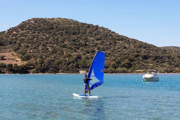 Ein Windsurfer am Strand mit einem Boot im Hintergrund.