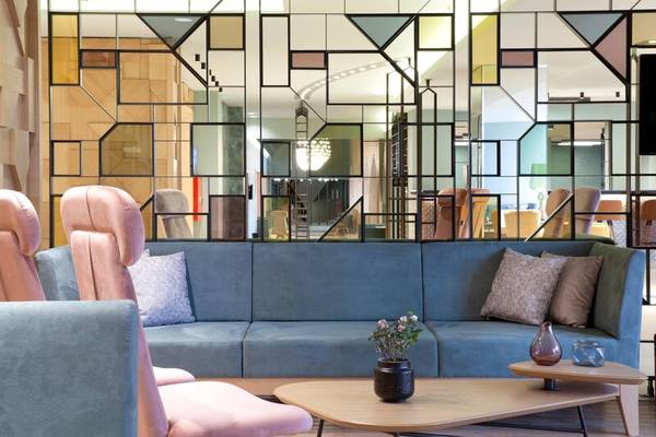 Lobby-Lounge-Bereich im Dolce Athens Attica Riviera mit blauer Couch, pinken Sesseln und geometrischen Wandspiegeln.