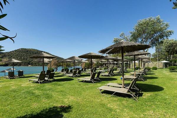 Hotelstrand mit vielen Sonnenliegen und Strohschirmen vor einem See.