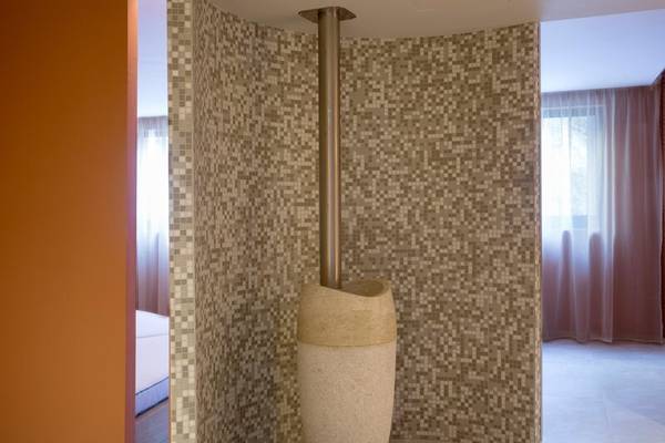 Innenansicht der Duschkabine im Dolce Athens Attica Riviera Hotel mit brauner Wandfliesen und einer freistehenden Dusche.
