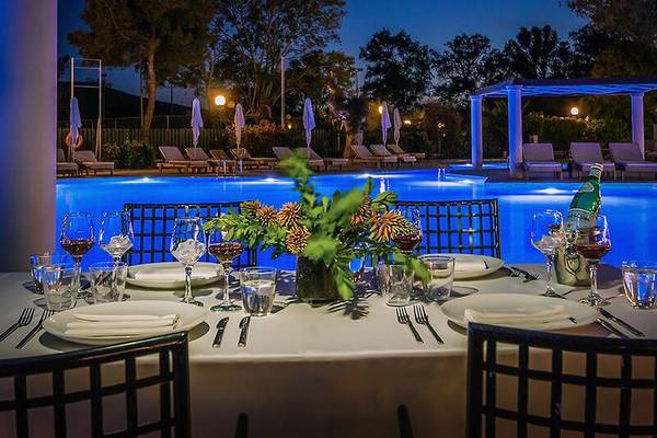 Poolseitiges Tisch-Setup im Dolce Athens Attica Riviera mit Wein und Pflanzen.