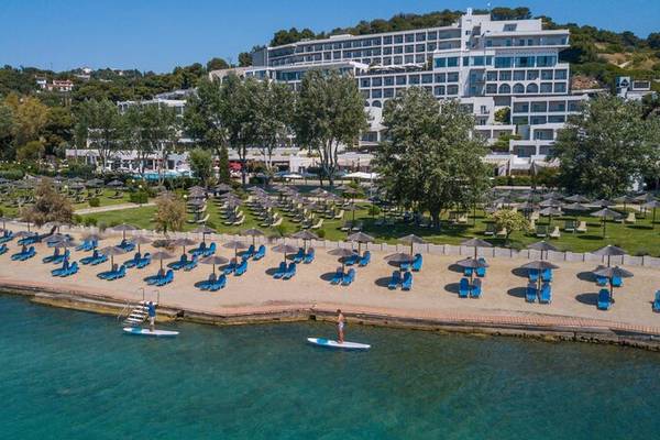 Luftaufnahme des Dolce Athens Attica Riviera Hotels mit vielen Sonnenliegen und Sonnenschirmen am Strand