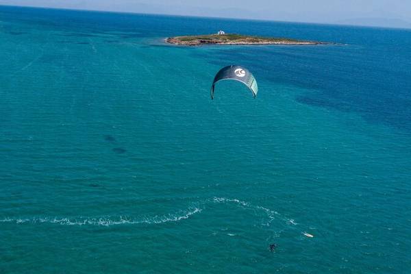 Ein Segelparaglider fliegt über dem blauen Meer mit einer kleinen Insel im Hintergrund.