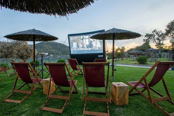 Gartenkino im Dolce Athens Attica Riviera Hotel mit roten Stühlen und Sonnenschirmen.