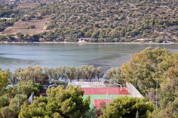 Aussicht auf einen Sportplatz mit zwei Tennisplätzen und einem Basketballplatz, umgeben von Bäumen, mit einem See im Hintergrund.