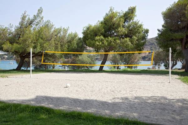 Strandvolleyballnetz mit Ball auf sandigem Boden mit Bäumen und Wasser im Hintergrund