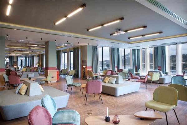 Innenbereich des Dolce Athens Attica Riviera Hotels mit bunten Möbeln und großen Fenstern.
