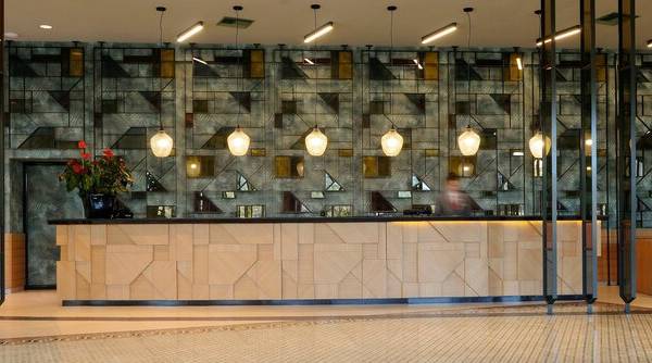 Empfangsbereich des Dolce Athens Attica Riviera Hotels mit moderner Wandgestaltung und Holzrezeptionstresen.