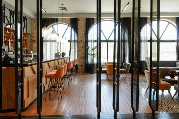 Innenbereich des Dolce Athens Attica Riviera Hotels mit Bar, Stühlen und großen Fenstern.