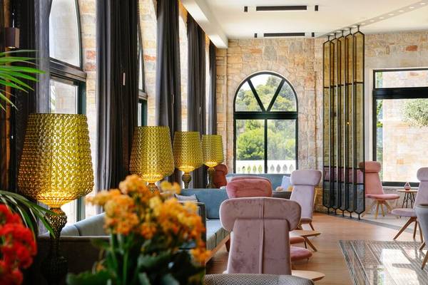 Innenbereich des Dolce Athens Attica Riviera Hotels mit Steinwand, bunten Stühlen und gelben Lampen.