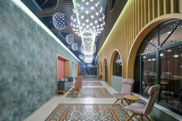 Der Innenbereich des Dolce Athens Attica Riviera Hotels mit gemusterten Wänden, einem Teppich und dekorativen Kronleuchtern.