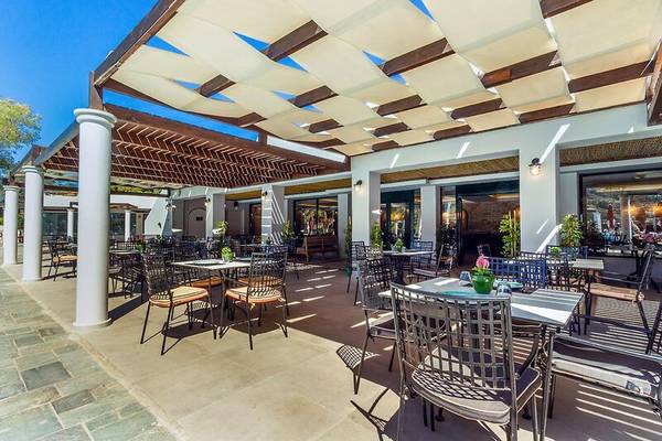 Außenbereich des Dolce Athens Attica Riviera Hotels mit Tisch und Stühlen unter einem Sonnendach.