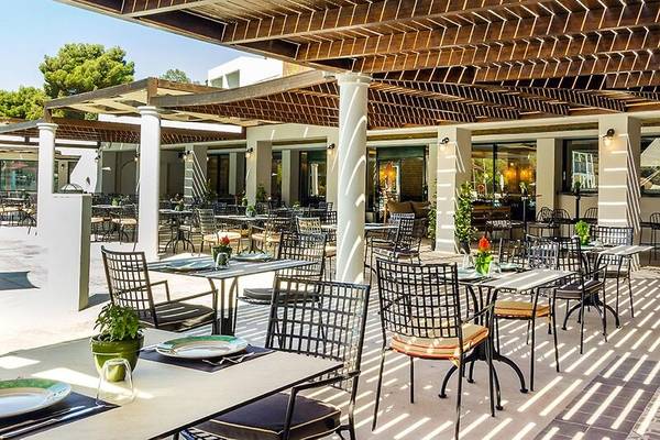 Terrasse des Dolce Athens Attica Riviera Hotels mit Tischen und Stühlen unter einer Pergola.