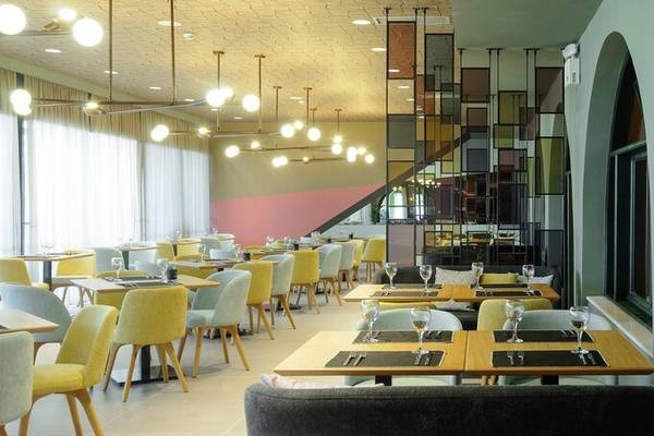 Innenansicht des Restaurants im Dolce Athens Attica Riviera Hotel mit gelb und grauen Stühlen und Tischen.