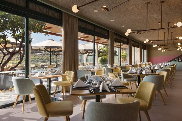 Restaurant im Dolce Athens Attica Riviera mit großen Fenstern und modernen Möbeln.