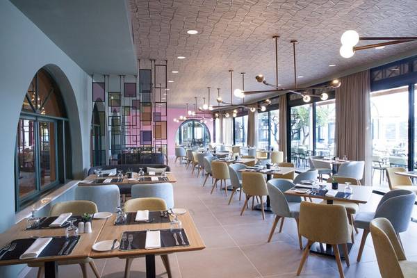 Innenansicht des Restaurants im Dolce Athens Attica Riviera Hotel mit modernen Möbeln und großen Fenstern.