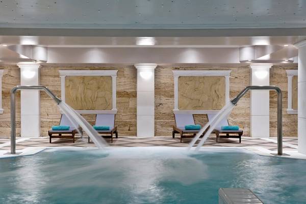 Poolbereich im Dolce Athens Attica Riviera Hotel mit Wasserstrahlen und Lounge-Sesseln.