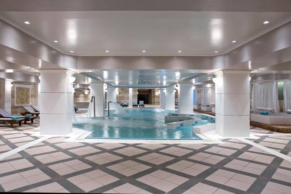 Innenpool im Dolce Athens Attica Riviera Hotel mit Wasserrutsche und Liegestühlen.