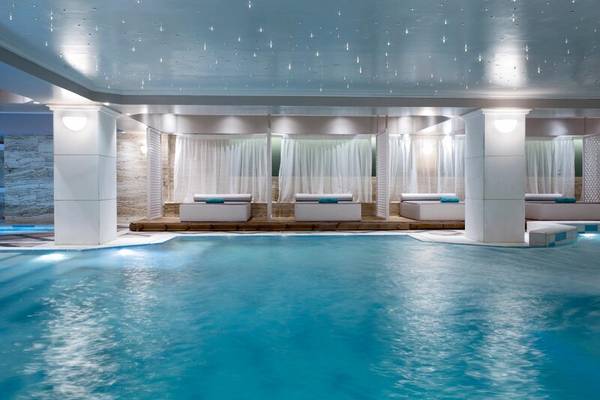 Ein modernes Schwimmbad im Dolce Athens Attica Riviera Hotel mit weißen Liegen und blauem Wasser.