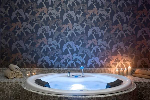 Jacuzzi im Dolce Athens Attica Riviera mit baummusterter Wand und beleuchteten Kerzen