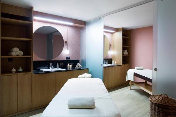 Massageraum im Dolce Athens Attica Riviera mit zwei Behandlungstischen und Holzmöbeln.