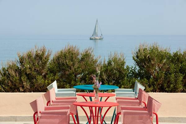 Terrasse des I Resort Beach Hotel & Spa mit Blick auf das Meer und ein Segelboot im Hintergrund