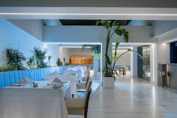 Das geräumige Restaurant des I Resort Beach Hotel & Spa mit weißen Tischen, blauen Bänken und großen Pflanzen in weißen Töpfen.