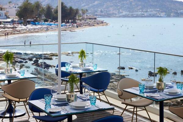 Terrasse des I Resort Beach Hotel mit Blick auf das Meer, wo mehrere blaue Tische und Stühle aufgestellt sind.